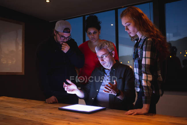Вид спереду на різноманітну групу творців за столом в офісній конференц-залі, дивлячись на планшетний комп'ютер в обговоренні на зустрічі — стокове фото