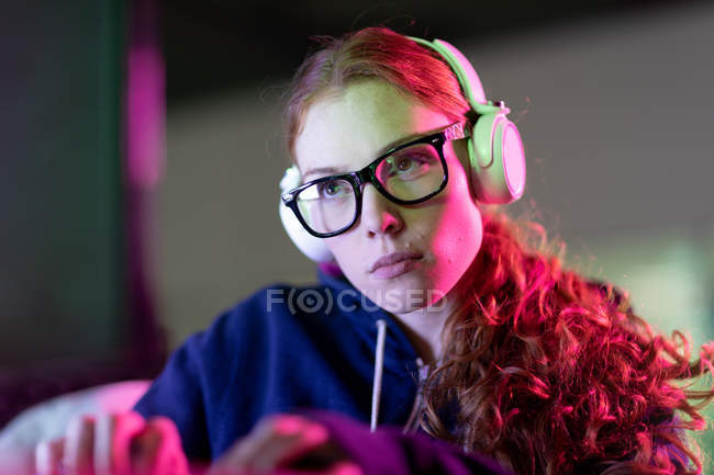 Vorderansicht einer jungen kaukasischen Frau, die in einem kreativen Büro arbeitet, eine Brille trägt und mit Kopfhörern Musik hört — Stockfoto