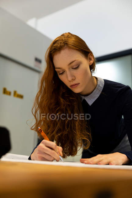 Front view close up of a young Caucasian woman working in a creative office, standing by her desk, concentrating. — Stock Photo