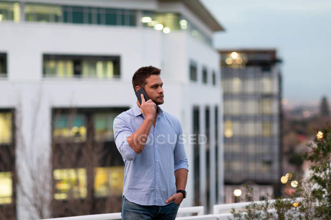 Передній вигляд молодого кавказького професіонала, який працював у сучасному офісі, стоїть на терасі даху за допомогою смартфона. — стокове фото