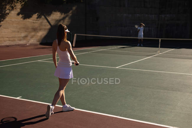 Вид сзади на молодую кавказскую женщину и мужчину, играющих в теннис в солнечный день, отдыхающих на корте — стоковое фото