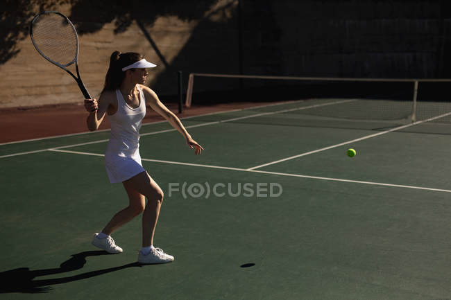 Vista laterale di una giovane donna caucasica che gioca a tennis in una giornata di sole, colpendo una palla — Foto stock