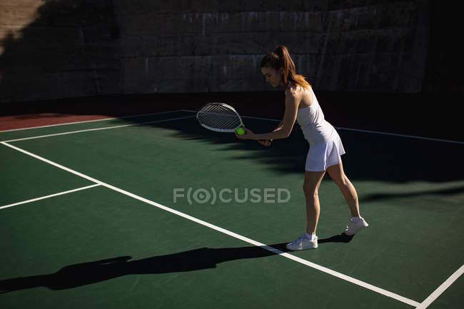 Vista laterale della donna che gioca a tennis in una giornata di sole, preparandosi a servire con un muro dietro di lei — Foto stock