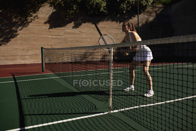 Vista laterale di una giovane donna caucasica che gioca a tennis in una giornata di sole, tiene in mano una racchetta e aspetta la palla — Foto stock
