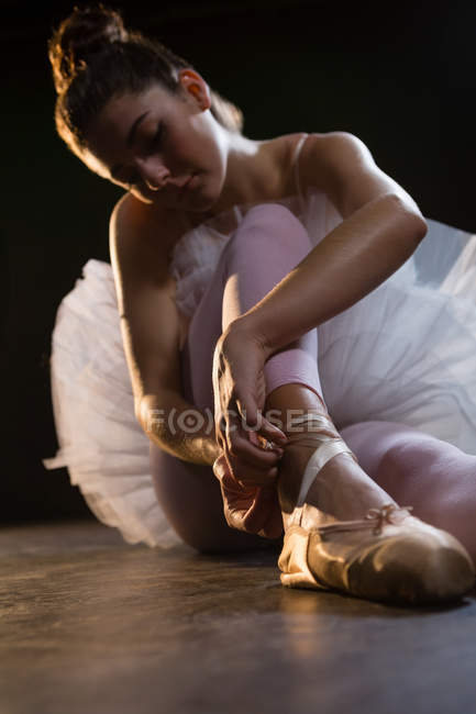Dançarina de ballet feminina amarrando a fita em seus sapatos de balé no estúdio — Fotografia de Stock