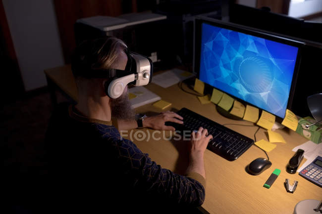 Ejecutivo usando auriculares de realidad virtual mientras trabaja en el escritorio en la oficina - foto de stock