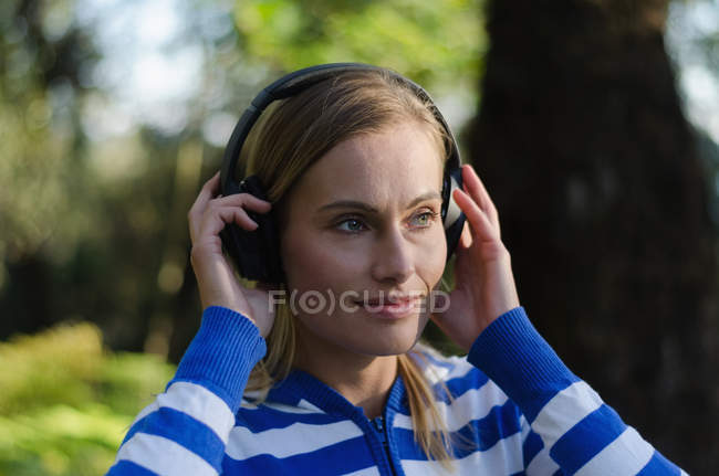 Primer plano de la excursionista escuchando música mientras está de pie en el bosque - foto de stock