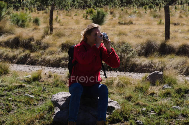 Жінка-пішохід фотографування, сидячи на скелі в лісі — стокове фото