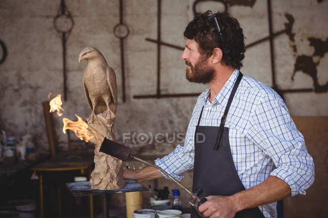 Задумчивый ремесленник смотрит на скульптуру птицы в мастерской — стоковое фото