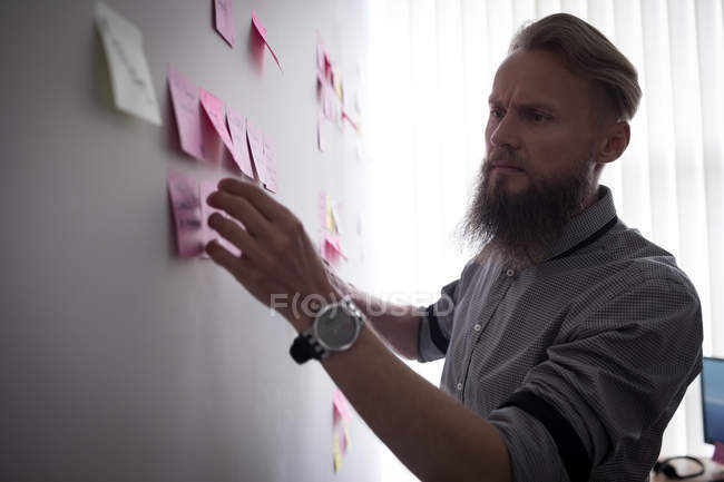 Attentive executive reading sticky notes in office — Stock Photo