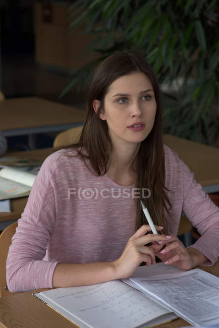 Thoughtful young college student studying at desk in classroom — Stock Photo