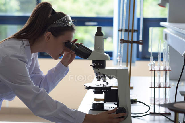 Vista lateral de una joven estudiante usando microscopio en el laboratorio - foto de stock
