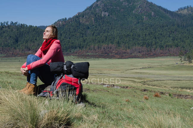 Comprimento total de caminhante feminino olhando para cima enquanto sentado na rocha contra a montanha — Fotografia de Stock