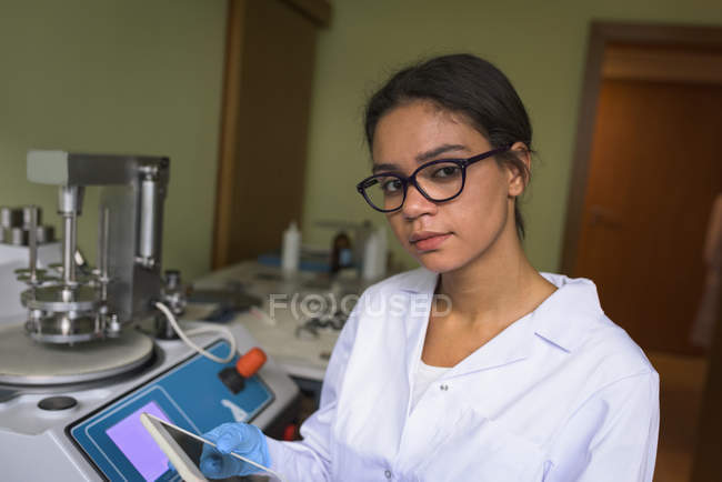 Portrait of teenage girl holding tablet while sitting by machinery in lab — Stock Photo