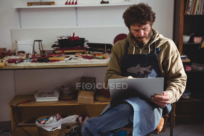 Майстер використовує ноутбук, сидячи в майстерні — стокове фото