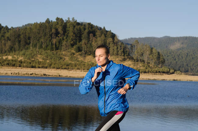 Female athlete running by lake against sky — Stock Photo
