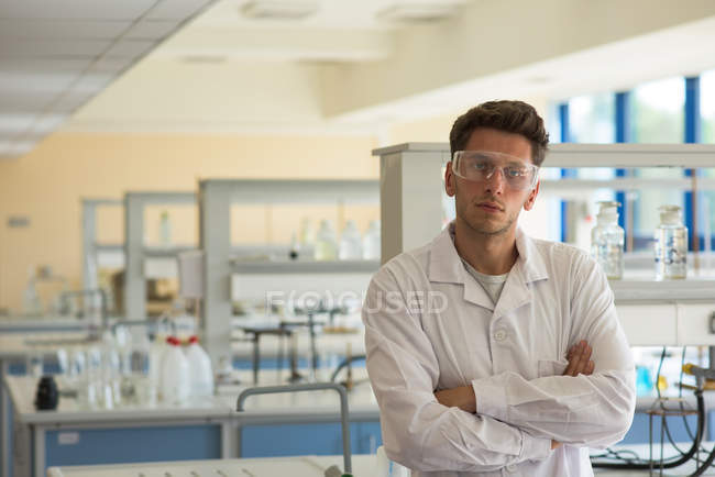Ritratto di studente universitario maschio con le braccia incrociate in piedi in laboratorio — Foto stock