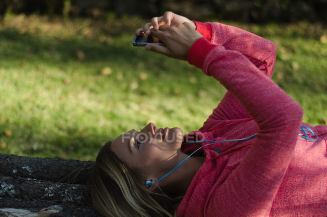 Крупним планом жіночий пішохід, використовуючи телефон, лежачи на підпірній стіні в лісі — стокове фото