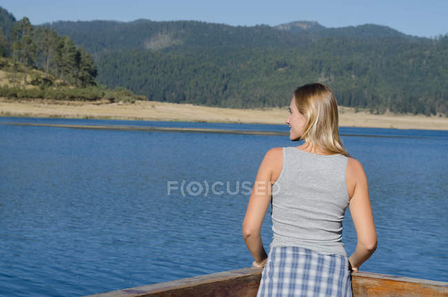 Vista trasera del excursionista femenino de pie junto a la barandilla en el muelle contra la montaña - foto de stock