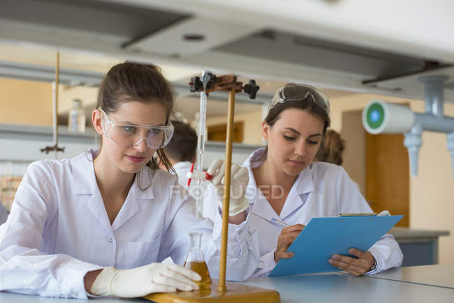 Estudiantes universitarias practicando experimento de química en laboratorio - foto de stock
