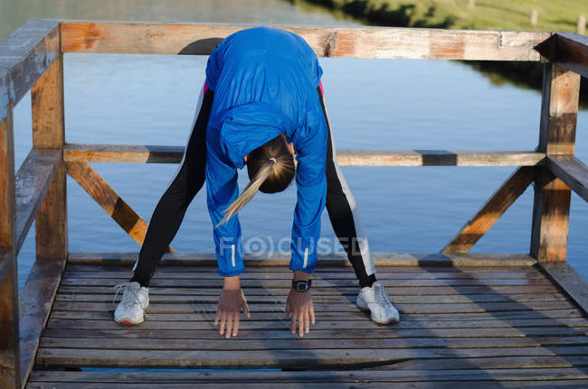 Tutta la lunghezza di atleta femminile che si esercita sul molo al lago — Foto stock