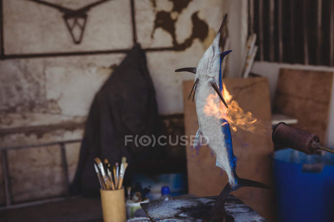Fish sculpture being heated by burner in workshop — Stock Photo