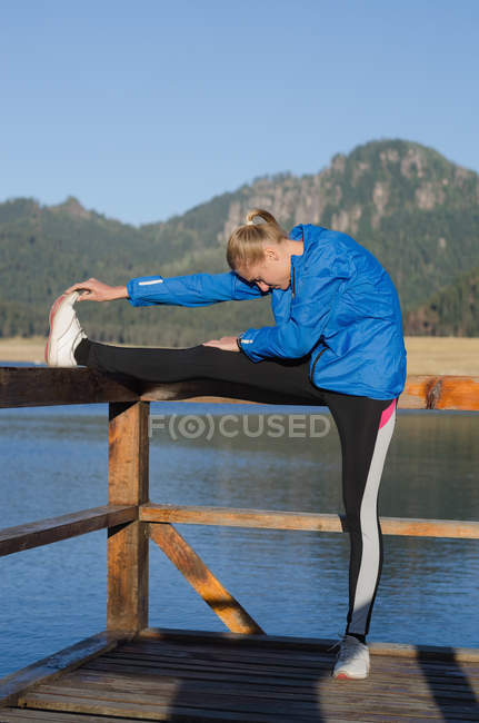 Jovem atleta se alongando enquanto se exercita no cais contra o céu limpo — Fotografia de Stock