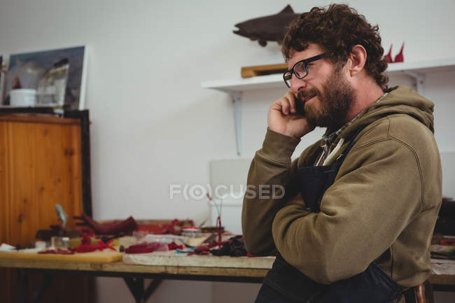 Craftsman talking on mobile phone in workshop — Stock Photo
