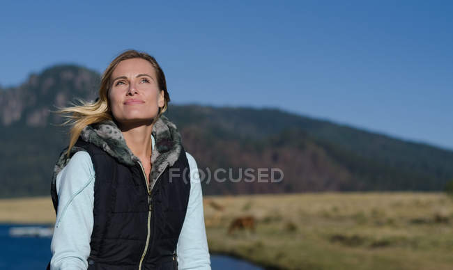 Усміхнена жінка дивиться геть, сидячи проти озера в сонячний день — стокове фото