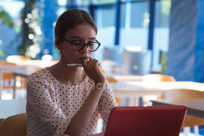Teenager-Studentin schaut auf Laptop, während sie am Schreibtisch im Klassenzimmer lernt — Stockfoto