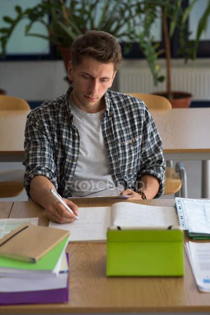 Vista de ángel alto de hombre joven usando tableta digital mientras está sentado en el escritorio en el aula - foto de stock