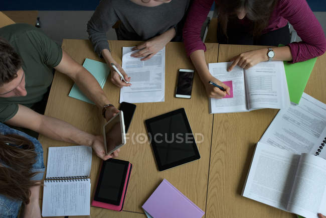 Vista de alto ángulo de los estudiantes universitarios que estudian en el escritorio en el aula - foto de stock