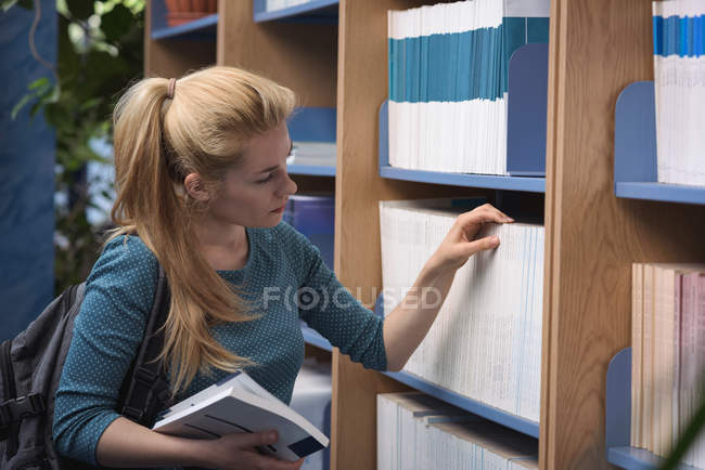Estudiante universitario seleccionando libro de la biblioteca en la universidad - foto de stock