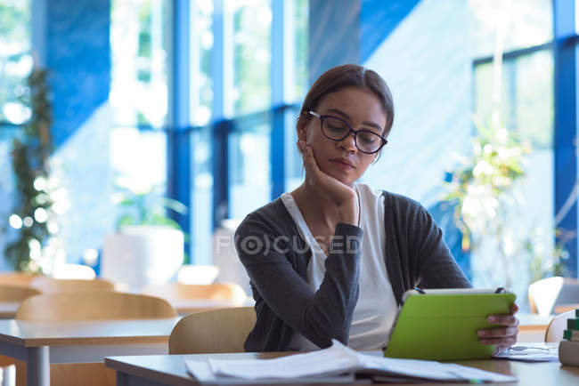 Adolescente com a mão no queixo usando o computador tablet enquanto sentado na mesa em sala de aula — Fotografia de Stock