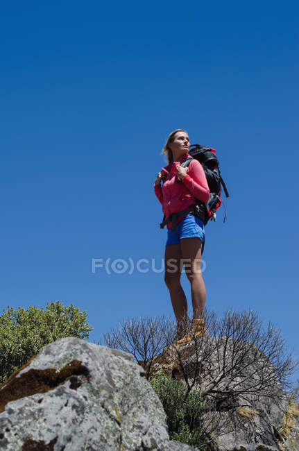 Vista angelical baja del excursionista femenino de pie sobre roca contra el cielo azul claro - foto de stock