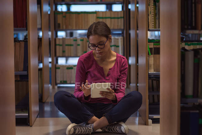 Дівчина-підліток використовує цифровий планшет, сидячи в бібліотеці — стокове фото