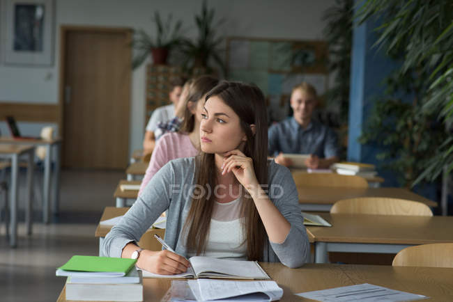 Thoughtful female college student at desk during exam in classroom — Stock Photo