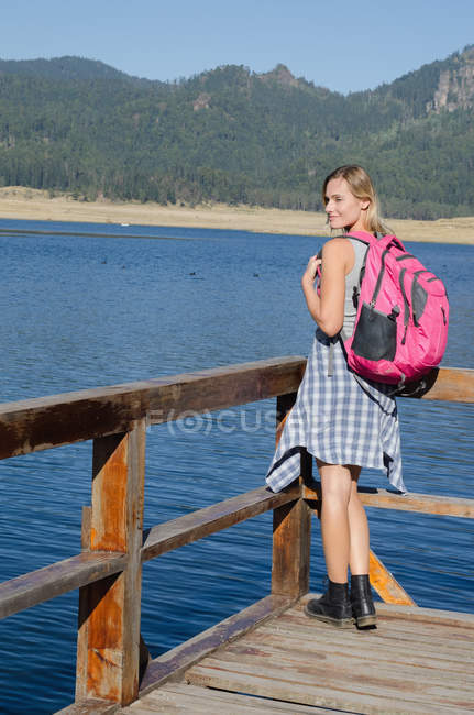 Rear view of female hiker with backpack standing by railing against mountain — Stock Photo