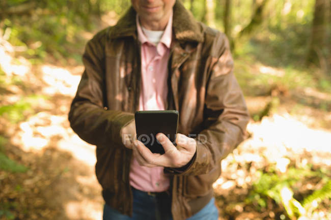 Середній розріз людини, що займається самовідливанням з мобільним телефоном у лісі. — стокове фото
