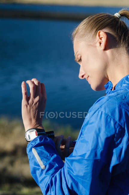 Vista lateral de la mujer que usa reloj de pulsera mientras está de pie contra el lago - foto de stock
