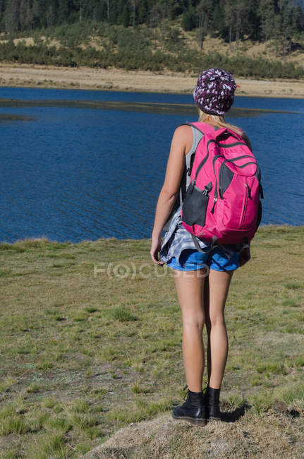 Rear view of female hiker standing on field against lake — Stock Photo