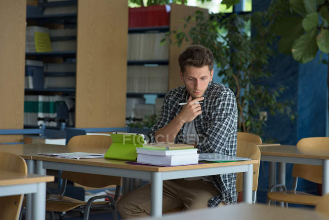 Giovane studente universitario maschio che studia alla scrivania in classe — Foto stock