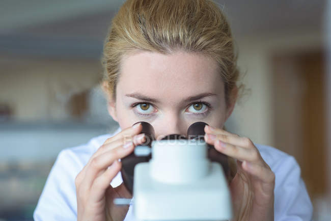 Retrato del estudiante universitario haciendo experimento con microscopio en laboratorio - foto de stock