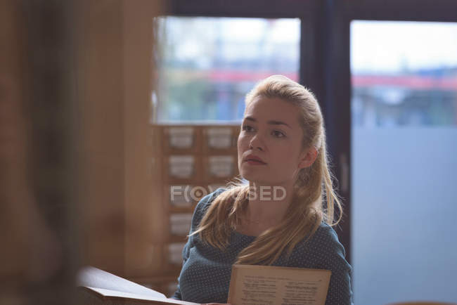 Nachdenkliches Mädchen liest Buch in Bibliothek am College — Stockfoto