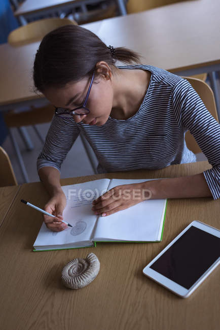 Vista de ángulo alto de la estudiante universitaria que practica el diagrama mientras estudia en el escritorio en el aula - foto de stock