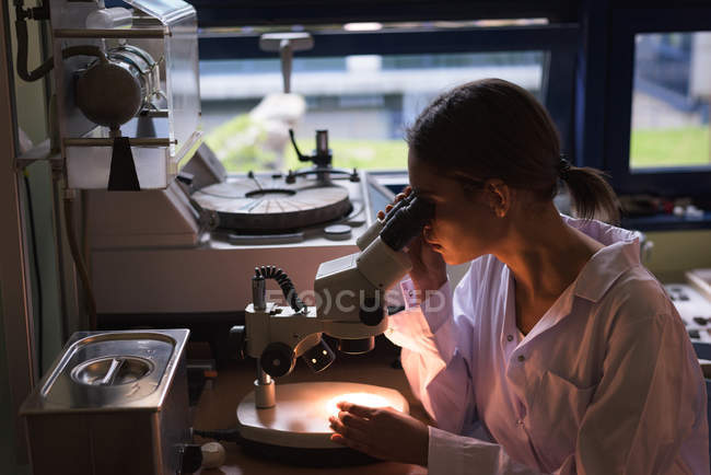 Female college student using microscope while practicing experiment in lab — Stock Photo