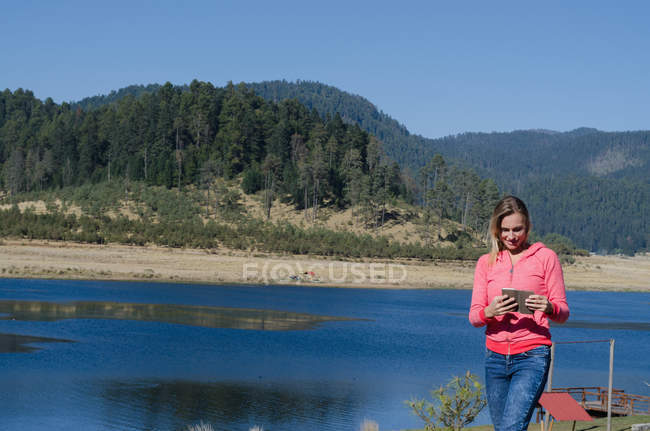 Female hiker using tablet while standing by lake against mountain — Stock Photo