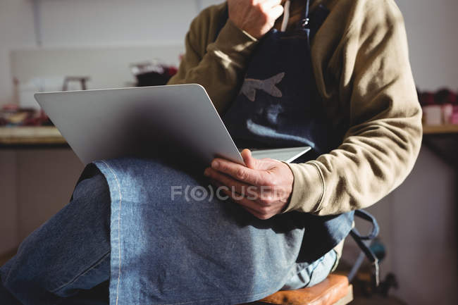 Mid-section of craftsman using laptop while sitting in workshop — Stock Photo