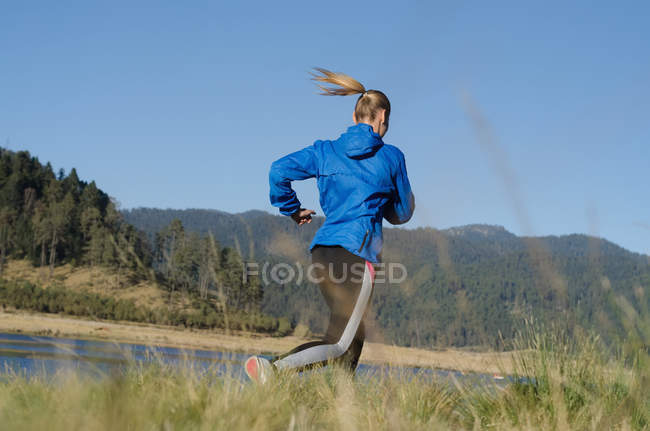 Rear view of female athlete running on field against clear blue sky — Stock Photo