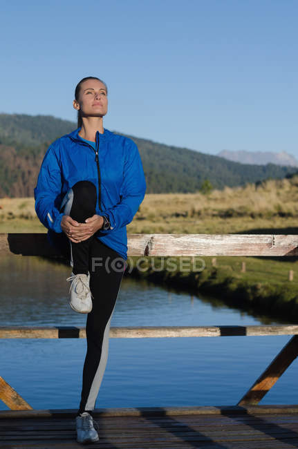 Спортсменка растягивается во время тренировки на пирсе у озера — стоковое фото